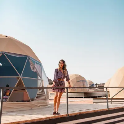 a woman standing next to a fence in front of tents at Thirteen Luxury Camp Valley in Wadi Rum