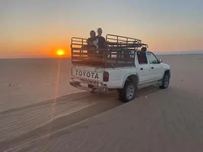 a group of people riding in the back of a truck in the desert at Halfway motel in An Namatah