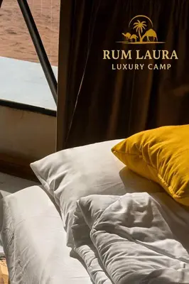 a bed with white sheets and a yellow pillow at Rum Laura luxury camp in Wadi Rum