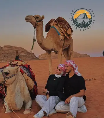 a man and woman sitting in the desert with a camel at WADI RUM BUBBlE AOSE CAMP in Wadi Rum