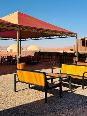 three yellow benches sitting under a red umbrella at Rum Dreamland luxury camp in Wadi Rum