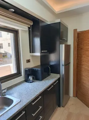 a kitchen with black cabinets and a stainless steel refrigerator at روف طابق ثاني تشطيب فندقي باطلاله ساحرة بعمارة عائلات بعبدون الشمالي in Amman