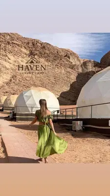 a woman in a green dress walking in front of a sign at Haven Luxury Camp in Aqaba