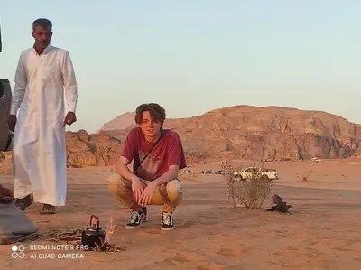 a man sitting next to a fire in the desert at Oasis of Wonders Camp in Wadi Rum