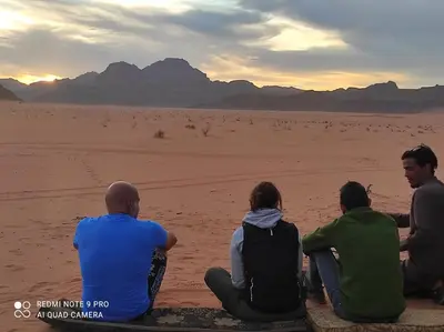 a group of people sitting in the desert watching the sunset at Oasis of Wonders Camp in Wadi Rum