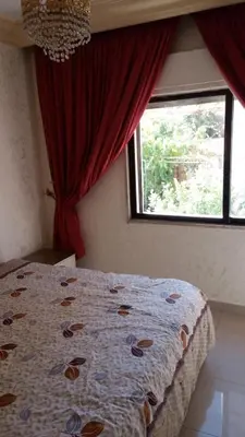 a bedroom with a bed and a window with red curtains at Al Khaleej Hotel Apartments in Amman