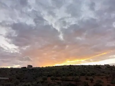 a cloudy sky with the sun setting on a hill at 1Happy farm in Al Salt