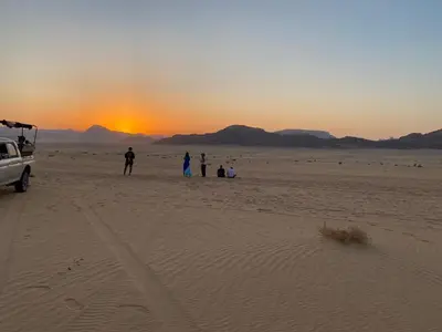 a group of people standing in the desert at sunset at Ahmad Wadi Rum Camp in Wadi Rum