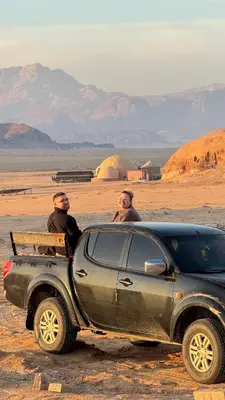 three men sitting next to a car in the desert at Wadi Ram camp in Disah