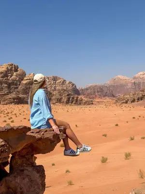 a woman sitting on a rock in the desert at Amjad Rum Camp in Disah