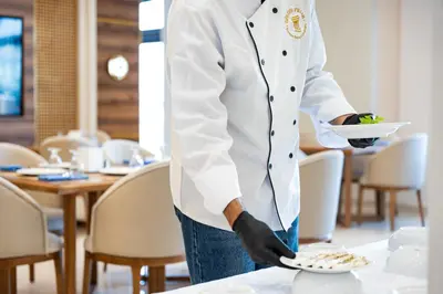 a chef holding a plate of food on a table at Golden Pillar Hotel in Aqaba