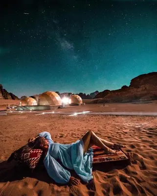 a man laying on a blanket on a beach at night at BUBBLES CAMp in Wadi Rum