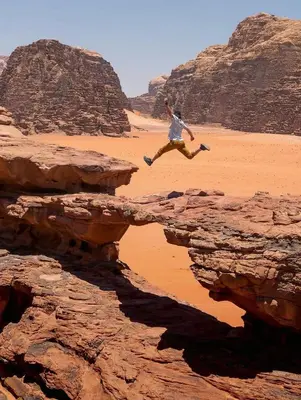 a man jumping over a cliff in the desert at Wadi Rum Moon Light in Wadi Rum