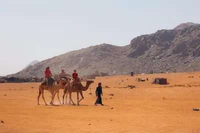 a group of people riding on camels in the desert at Rum Cave Tours in Wadi Rum