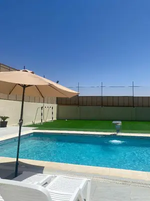 a swimming pool with an umbrella and a white chair at شاليه الدرة Durra Chalet in Amman