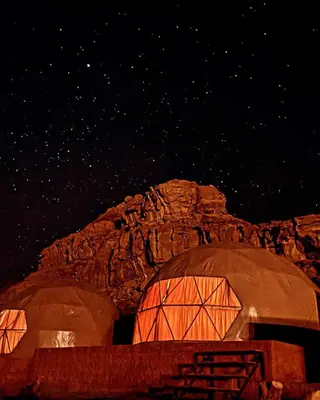a starry night with two domes in front of a mountain at Rum Rose Night in Wadi Rum