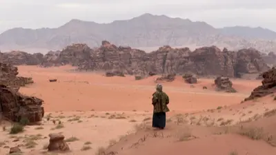 a man standing in a desert with mountains in the background at HALA RUM Luxury camp & Bubbles Hotel in Disah