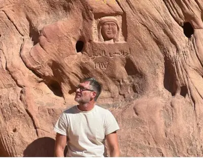 a man standing in front of a rock wall with a statue at Rum luxury camp hotel in Wadi Rum