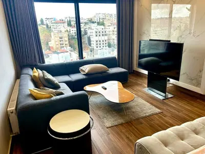 a living room with a blue couch and a large window at Elegant & Cozy Apartment in Heart of Amman in Amman