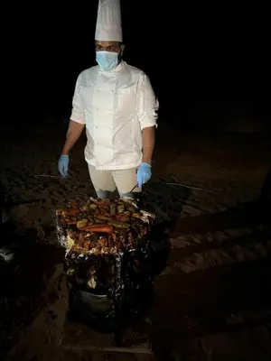 a chef standing next to a grill with food on it at TAJ luxury Camp in Wadi Rum