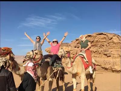 three people riding on camels in the desert at Essam camb in Disah