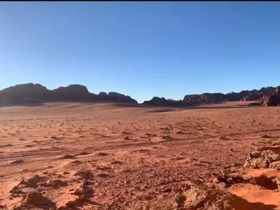 an empty desert with trees in the background at Enad wadirum camp in Wadi Rum