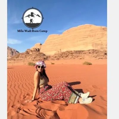 a woman sitting on the sand in the desert at Mila Wadi Rum Camp in Wadi Rum
