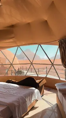 a woman laying on a bed in front of a window at Ahmad desert camp wadi rum in Wadi Rum