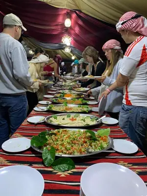 a group of people standing around a long table with plates of food at Hillawi Desert Camp Wadi Rum in Disah