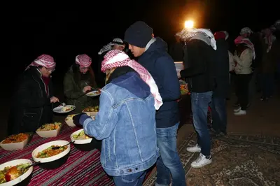 a group of people standing around a table with plates of food at Hillawi Private Bedouin Camp in Wadi Rum