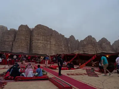 a group of people sitting on the beach in front of a mountain at Hillawi Private Bedouin Camp in Wadi Rum