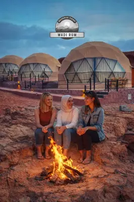 three women sitting around a fire in front of a building at WADI RUM RESERVE BUBBlE CAMP in Wadi Rum