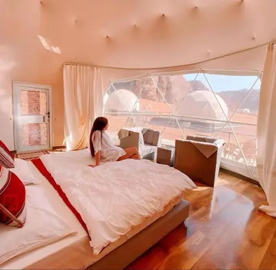a woman sitting on a bed in a room with a large window at Luxury Camp Wadi Rum in Disah