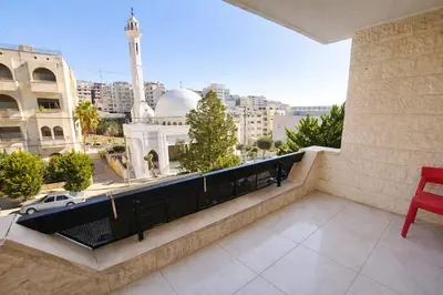 a balcony with a view of a mosque and a red chair at Wadi Saqra Family Apartment in Amman