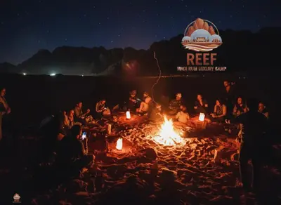 a group of people sitting around a fire on a beach at Reef Rum Luxury Camp in Disah