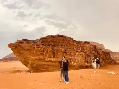 a group of people standing in front of a large rock at Wadi rum Nader in Aqaba