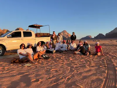 a group of people sitting in the sand next to a truck at Wadi Rum Star Sky in Wadi Rum