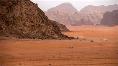 a car in the desert with mountains in the background at Skylight Wadi Rum Camp in Disah