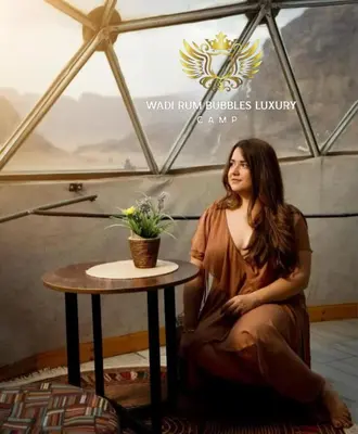 a woman sitting at a table in a room at WADI RUM BUBBLES lUXURY CAMP in Disah