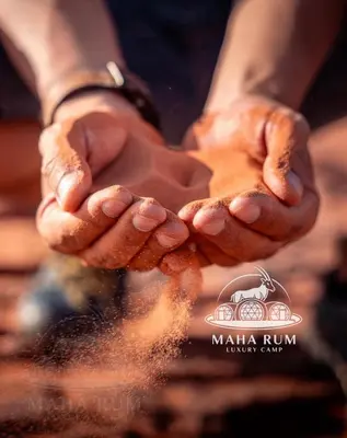 a person holding their hands out with sand pouring out at MAHA Rum Luxury Camp in Disah