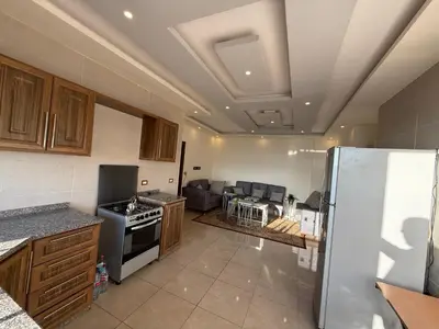 a kitchen with a refrigerator and a living room at شقة للإيجار في راس منيف - عجلون in Ajloun