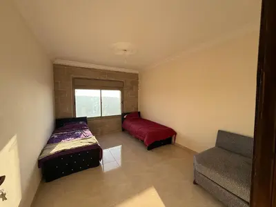a bedroom with two beds and a couch and a window at شقة للإيجار في راس منيف - عجلون in Ajloun