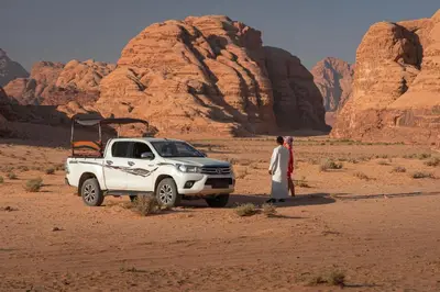 a woman standing next to a white truck in the desert at Wadi Rum Desert Night Camp in Wadi Rum