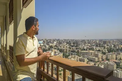 a man sitting on a balcony with a cup of coffee at Grand Hyatt Amman Residences in Amman