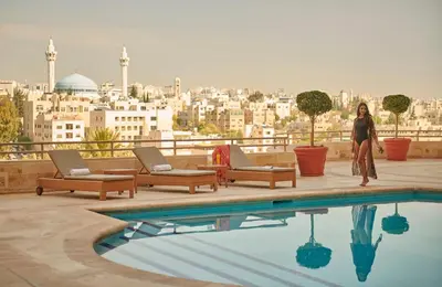 a woman standing next to a pool with a view of a city at Grand Hyatt Amman Residences in Amman