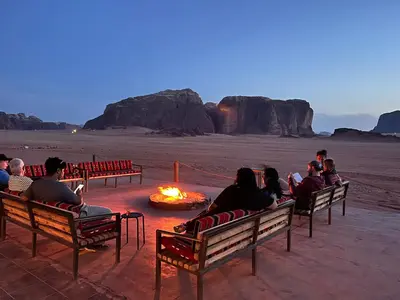 a group of people sitting around a fire in the desert at Wadi Rum Bedouin Camp in Wadi Rum