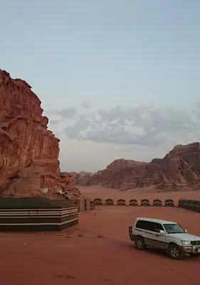 a white suv parked in a desert with mountains at Bedouin Traditions Camp in Wadi Rum