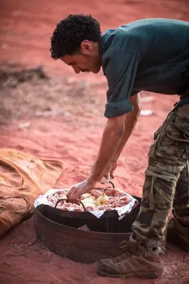 a man is making a pizza in a pan at Bedouin Traditions Camp in Wadi Rum