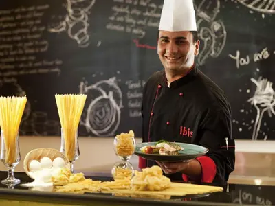 a chef holding a plate of food on a table at ibis Amman in Amman