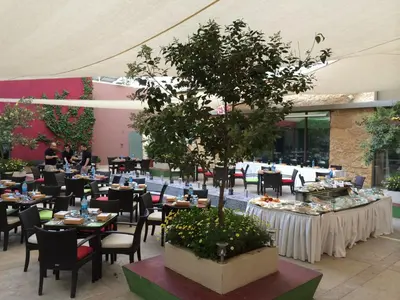 a restaurant with tables and chairs and a tree in the middle at ibis Amman in Amman